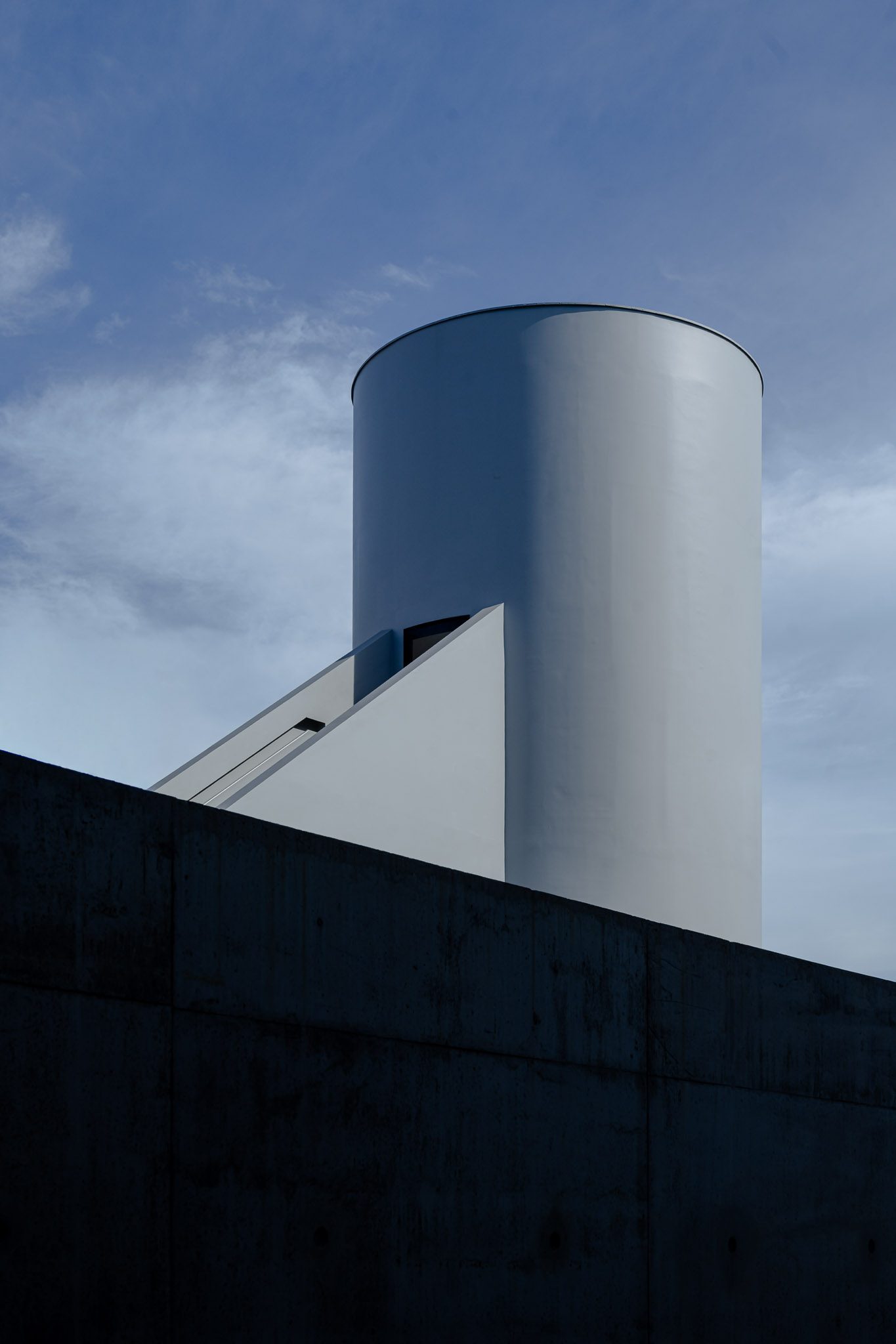 White cylindrical tower above a dark concrete wall, Dib Bangkok