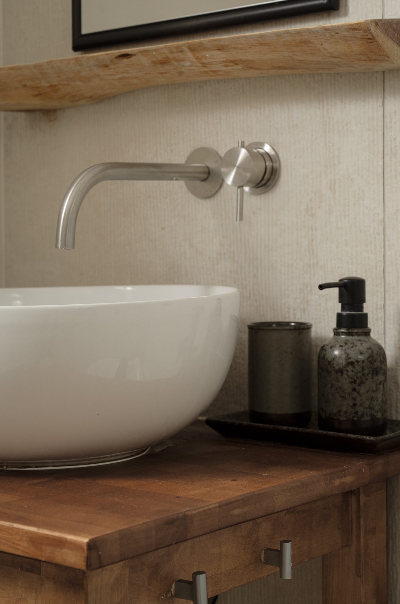 Wall-mounted tap above a white basin on walnut