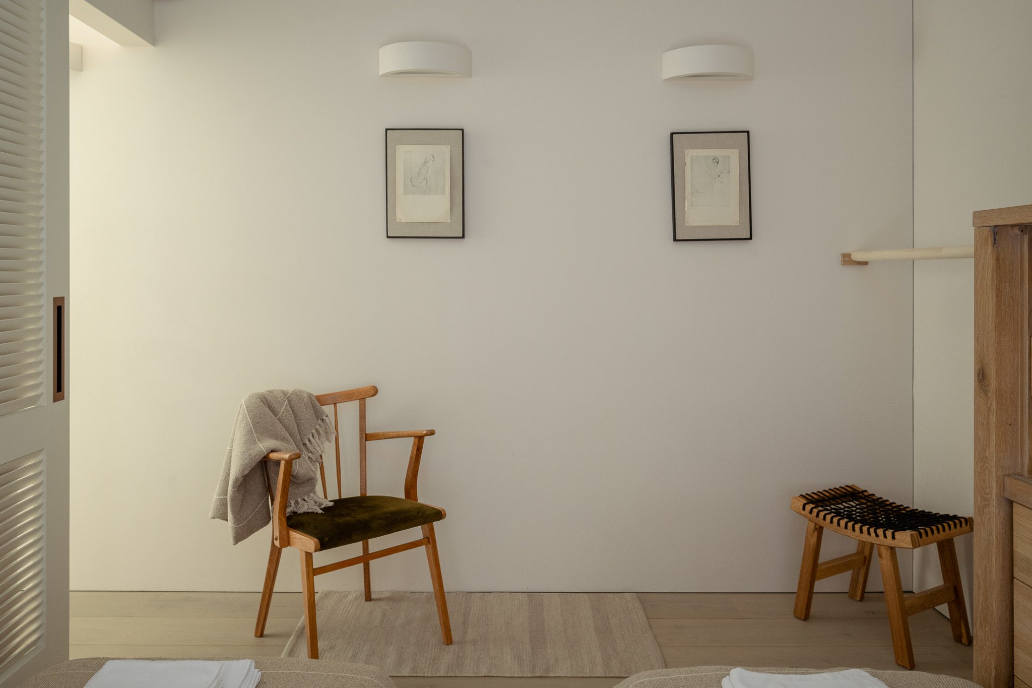 Chair and stool against a pale wall with framed prints