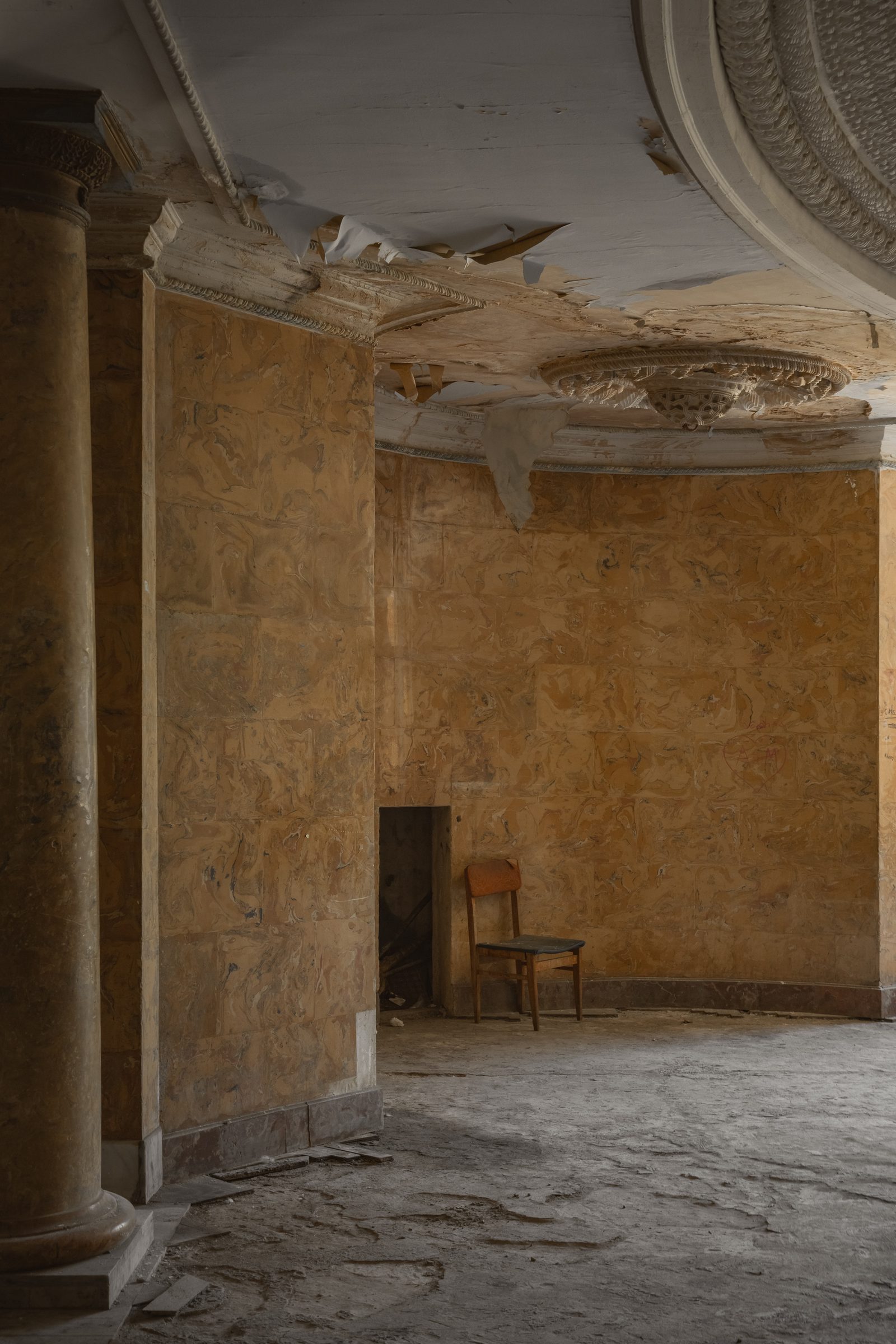 A single chair against an amber wall beneath a collapsing ceiling