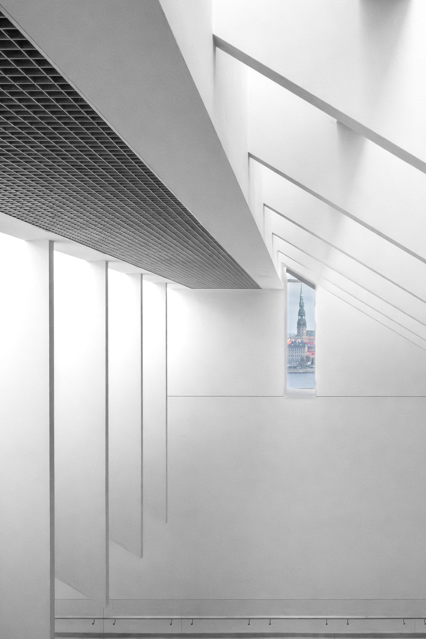White wall with a slit window framing the Riga skyline
