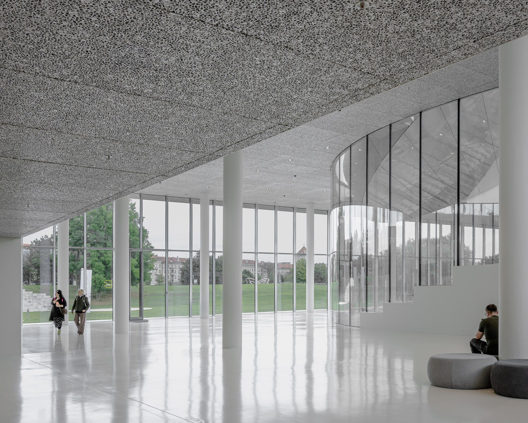 Visitors on the white ground floor beside the glass façade, Mokslo Sala