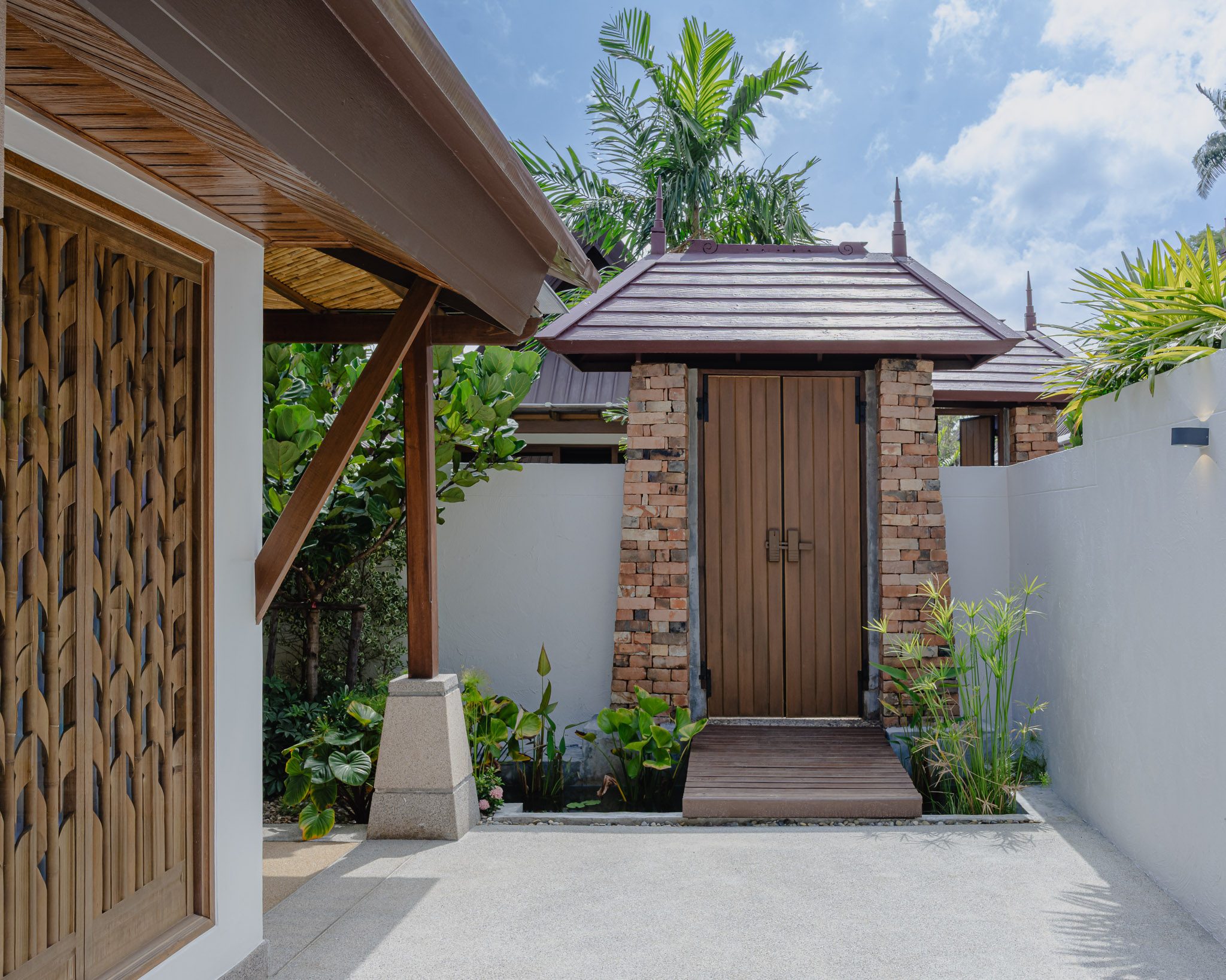 Carved timber gateway in a brick-and-plaster courtyard, Thai Cottage